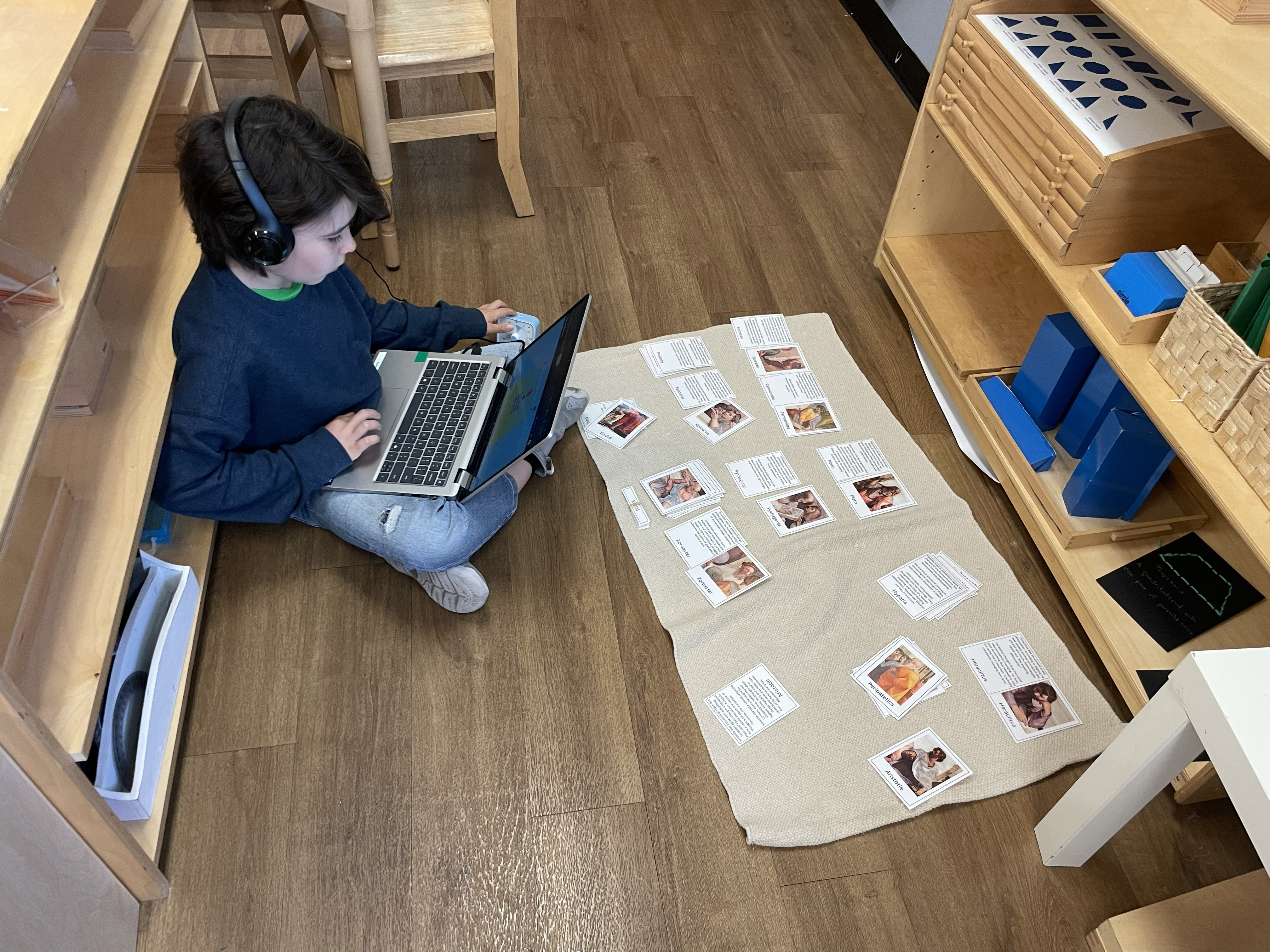 Student working on laptop with history picture cards laid out on rug